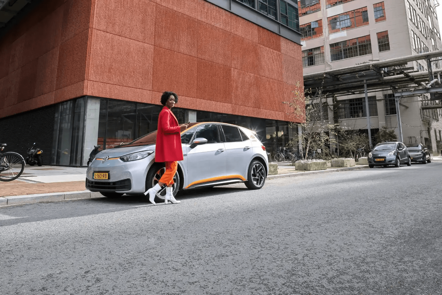 Woman in red coat walking dog past parked car on city street