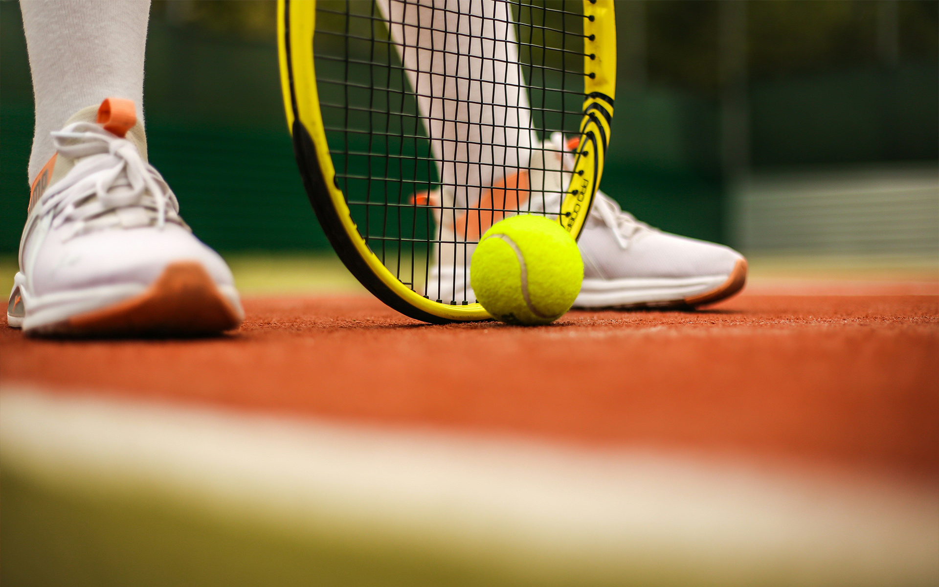 Close-up of tennis ball and racket on orange clay court