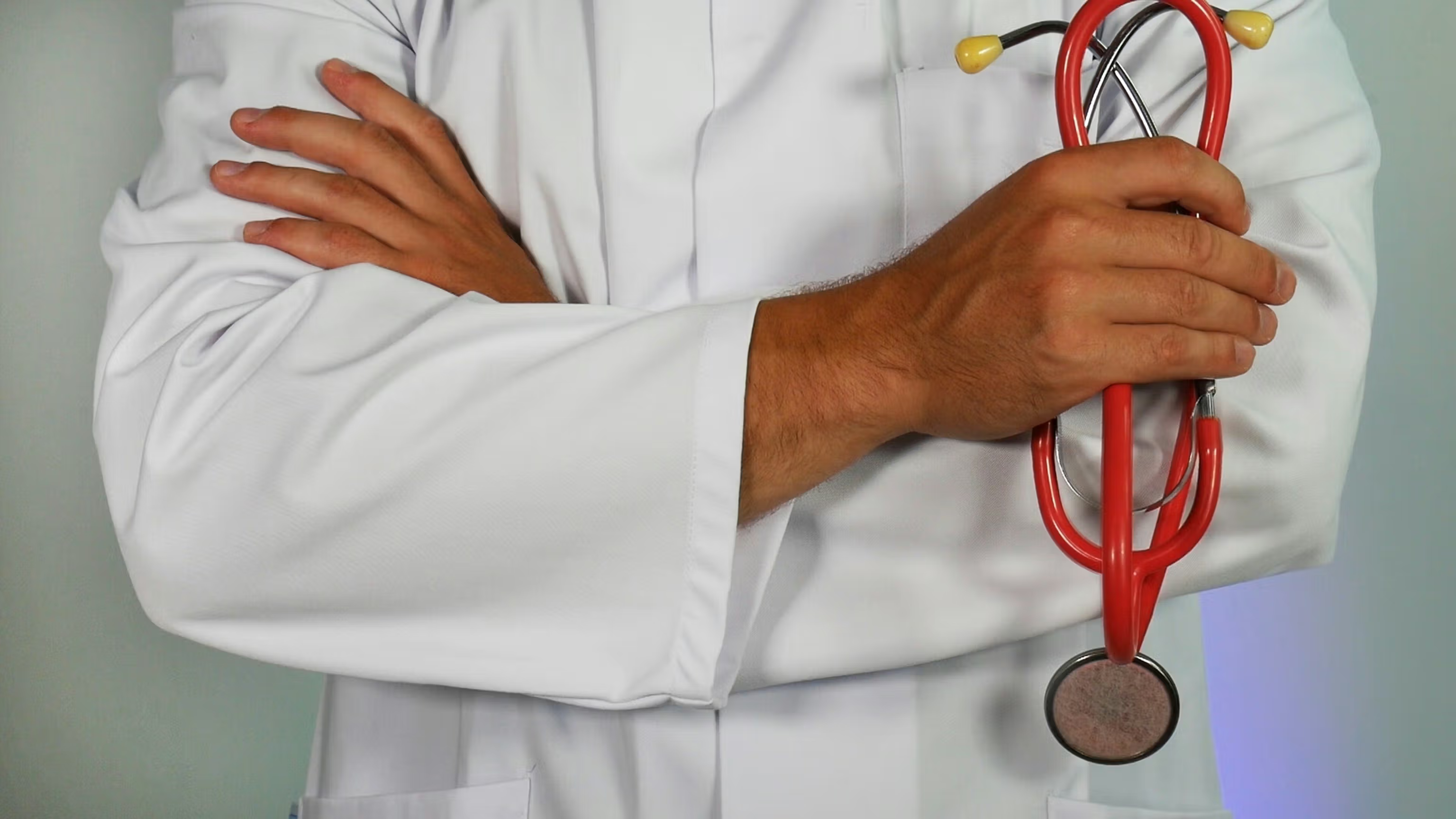 Doctor in white coat holding a red stethoscope with arms crossed