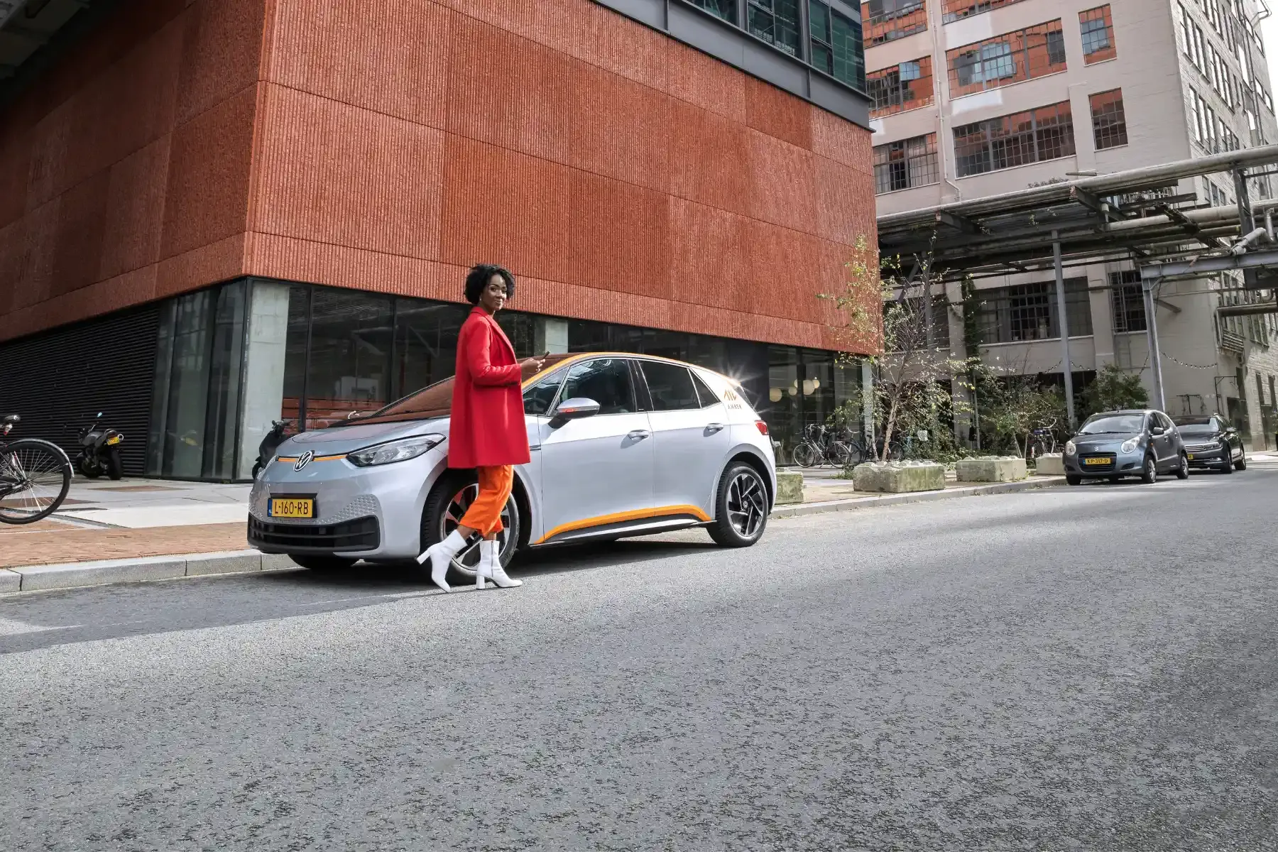 Woman in red coat walking dog past parked car on city street